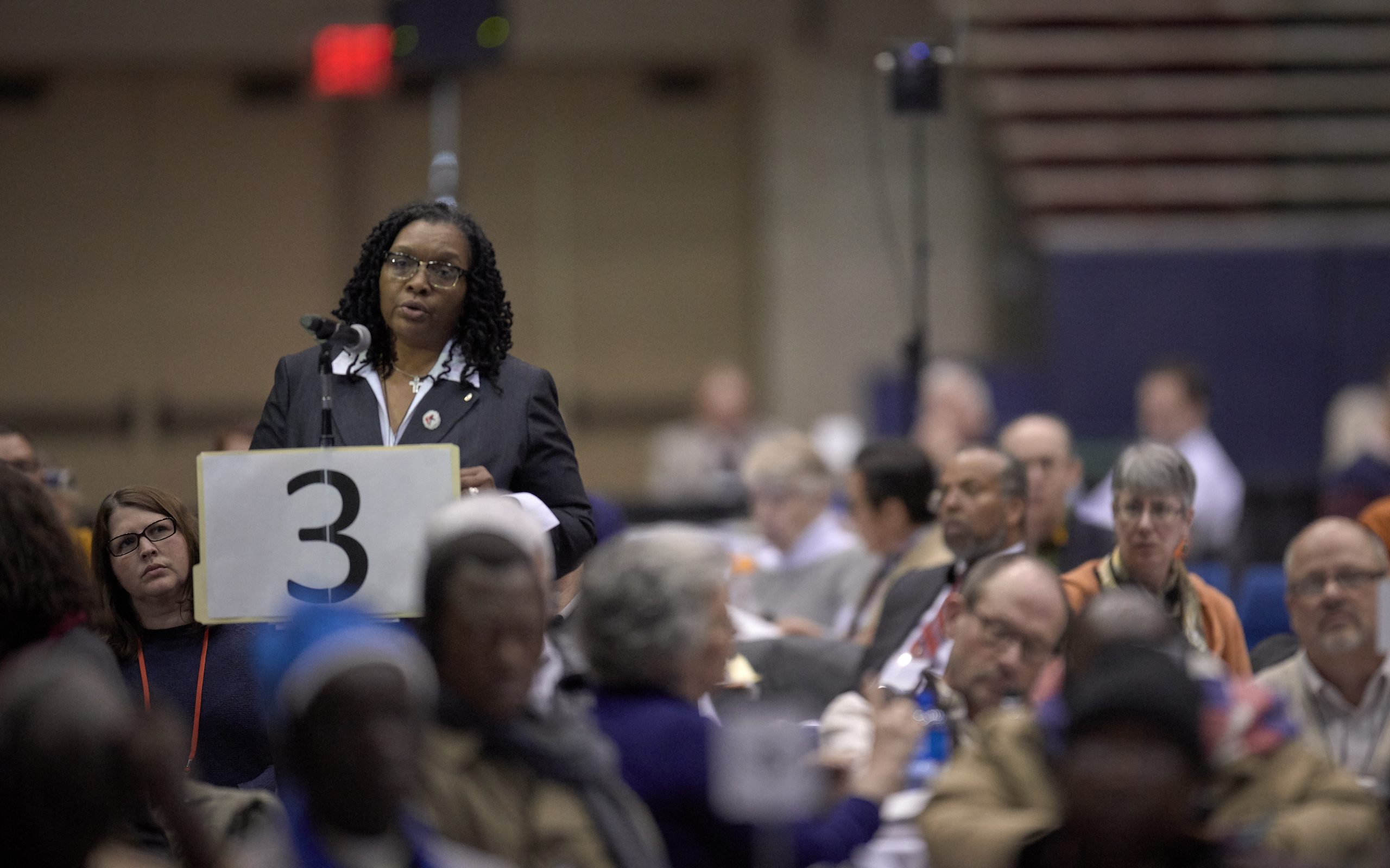 A woman stands at a microphone during a conference to speak