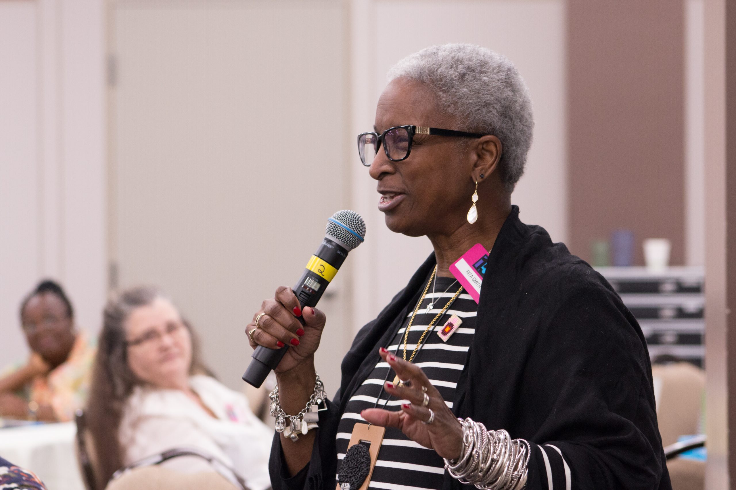 A woman smiles while speaking into a microphone during a meeting